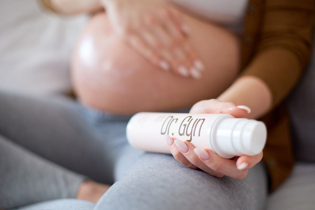 Eine schwangere Frau massiert ihren großen Bauch mit Creme, in der Hand hält sie Dr. Gyn Babybauch Pflege gegen Schwangerschaftsstreifen