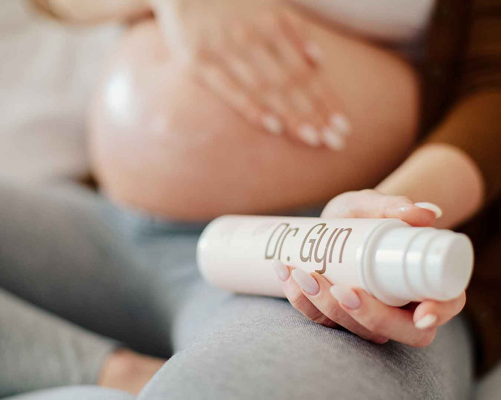 Nahaufnahme einer schwangeren Person, die sanft eine Creme mit der Aufschrift „Dr. Gyn” auf ihren Bauch aufträgt. Die Szene vermittelt ein Gefühl von Fürsorge und Pflege.