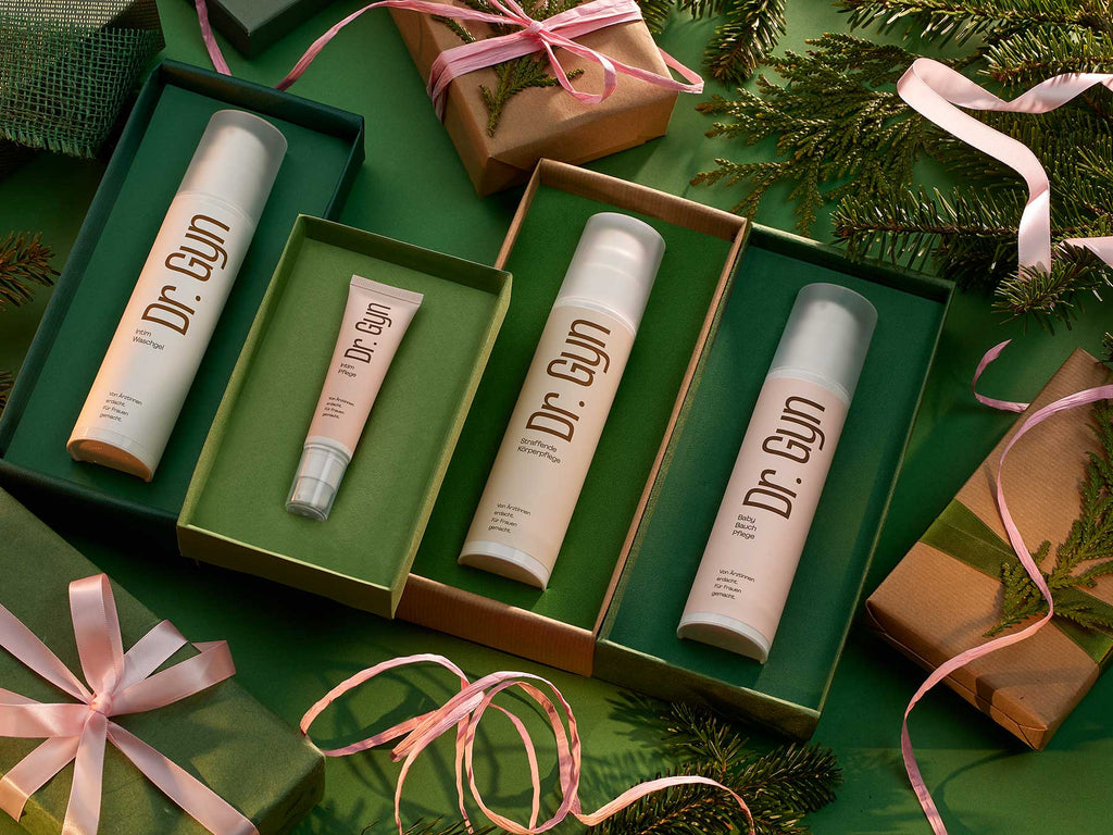 „Dr. Gyn“ Haut- und Intimpflegeprodukte als Weihnachtsgeschenk,  umgeben von rosa Bändern und weihnachtlichen Tannenzweigen. 